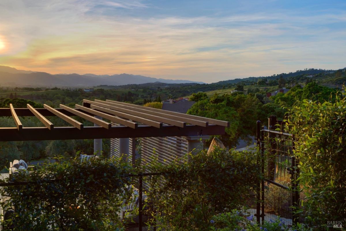 A pergola structure over a lush garden with a view of the surrounding landscape.