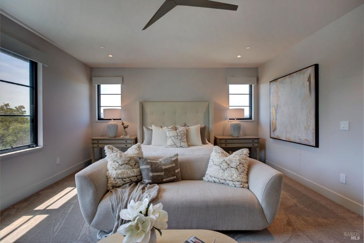 Bedroom with a tufted headboard, two side tables, a cozy loveseat at the foot of the bed, and simple decor.