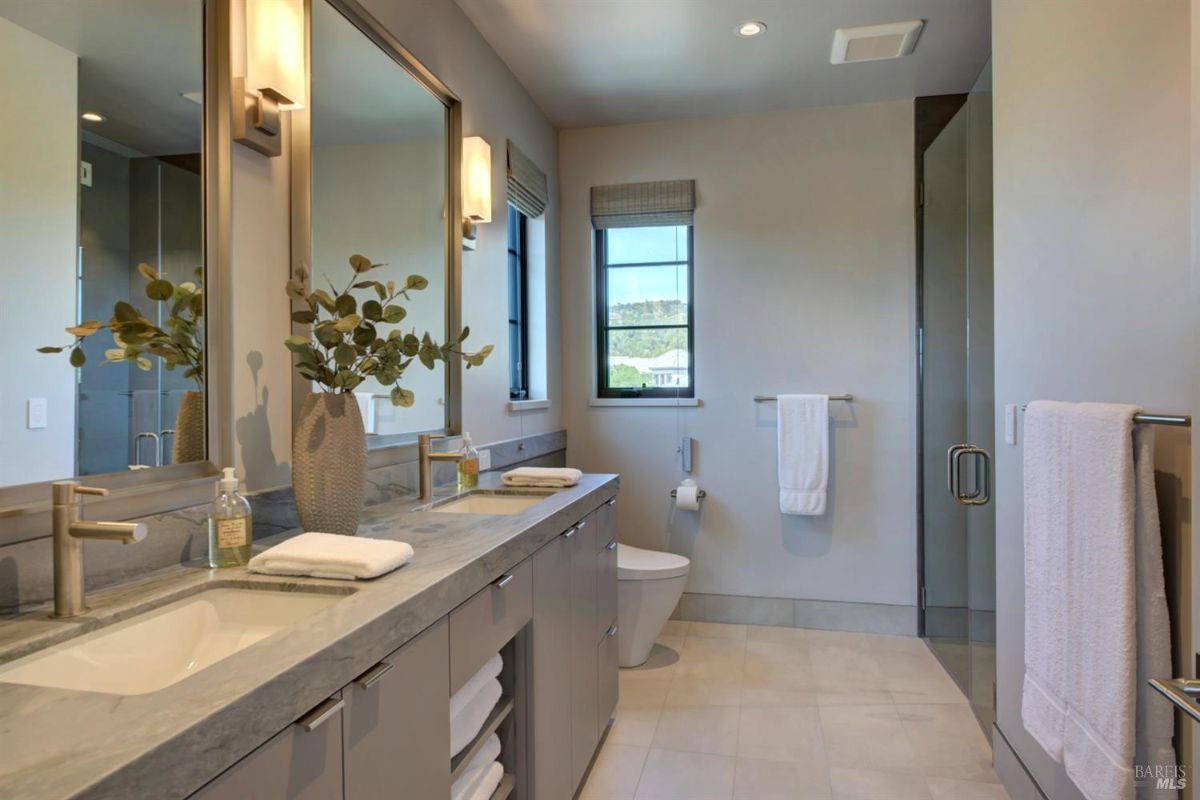 Bathroom with dual sinks, a large mirror, modern fixtures, and a shower visible in the background.