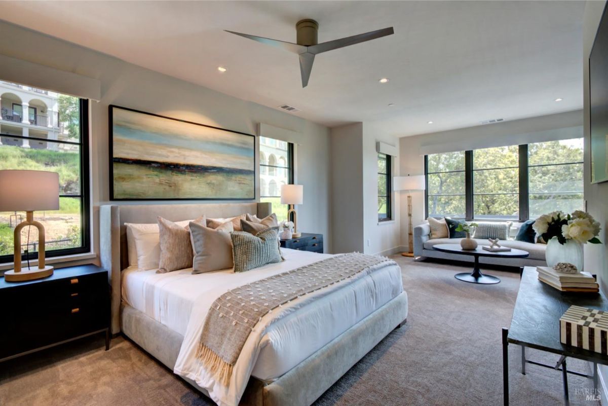 Bedroom with a king-size bed, large windows, a seating area, and a nature-inspired wall art piece.