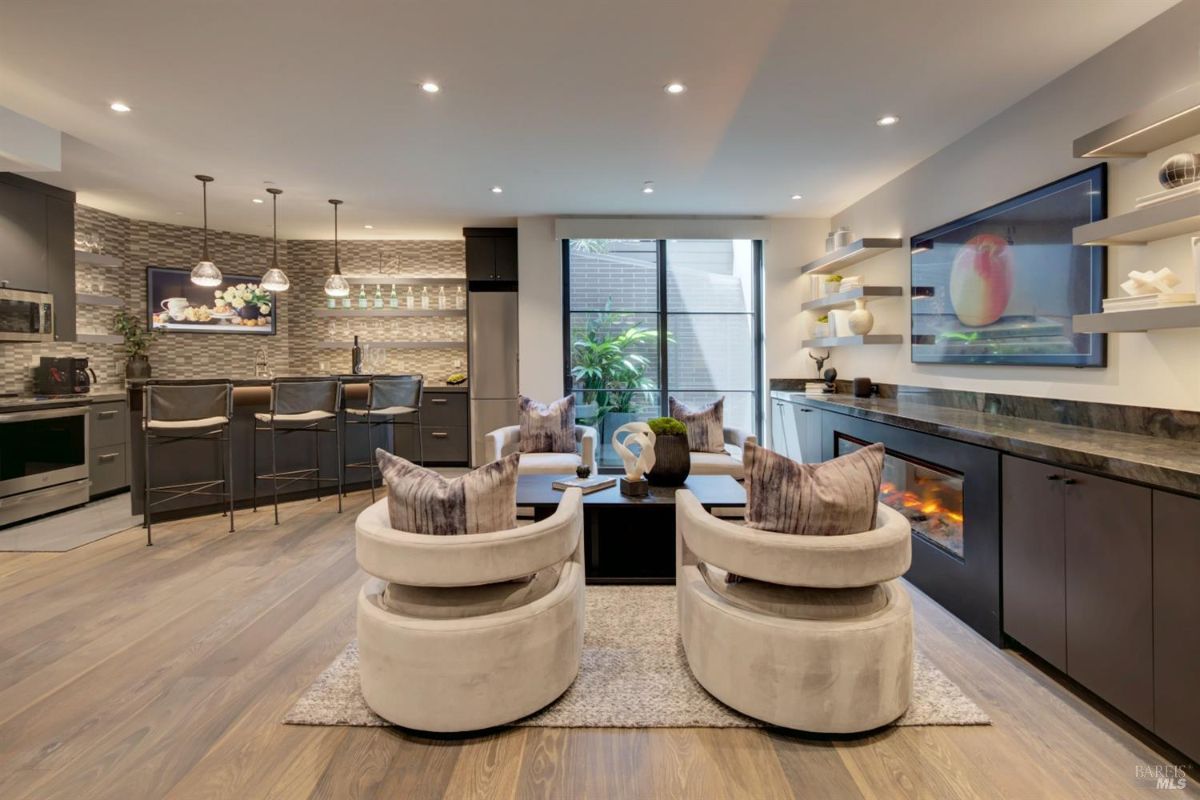 Living area with a modern kitchen, bar seating, and open shelving complemented by a fireplace.