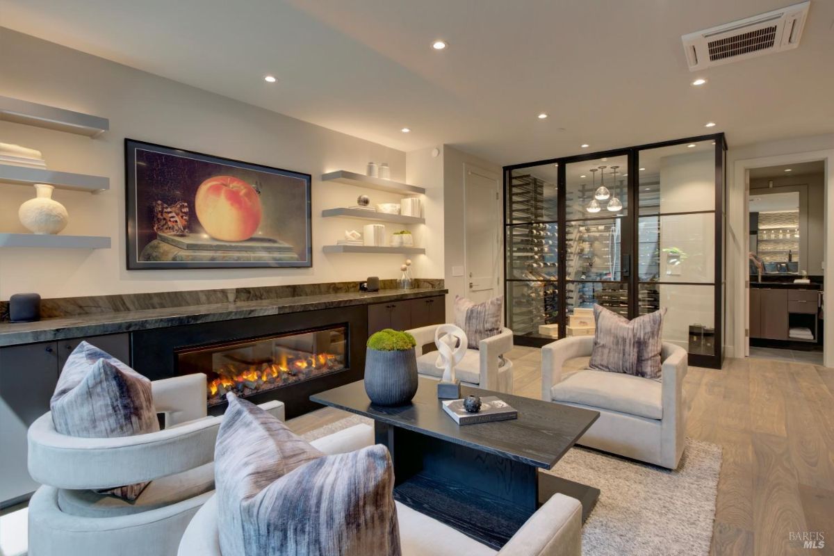 A sitting room with a modern fireplace, built-in shelving, and a glass-enclosed wine storage area in the background.