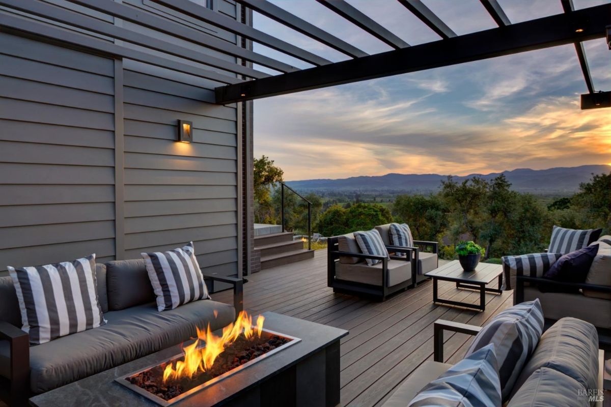 Outdoor seating area with a fire pit, comfortable chairs, and a pergola with scenic views.