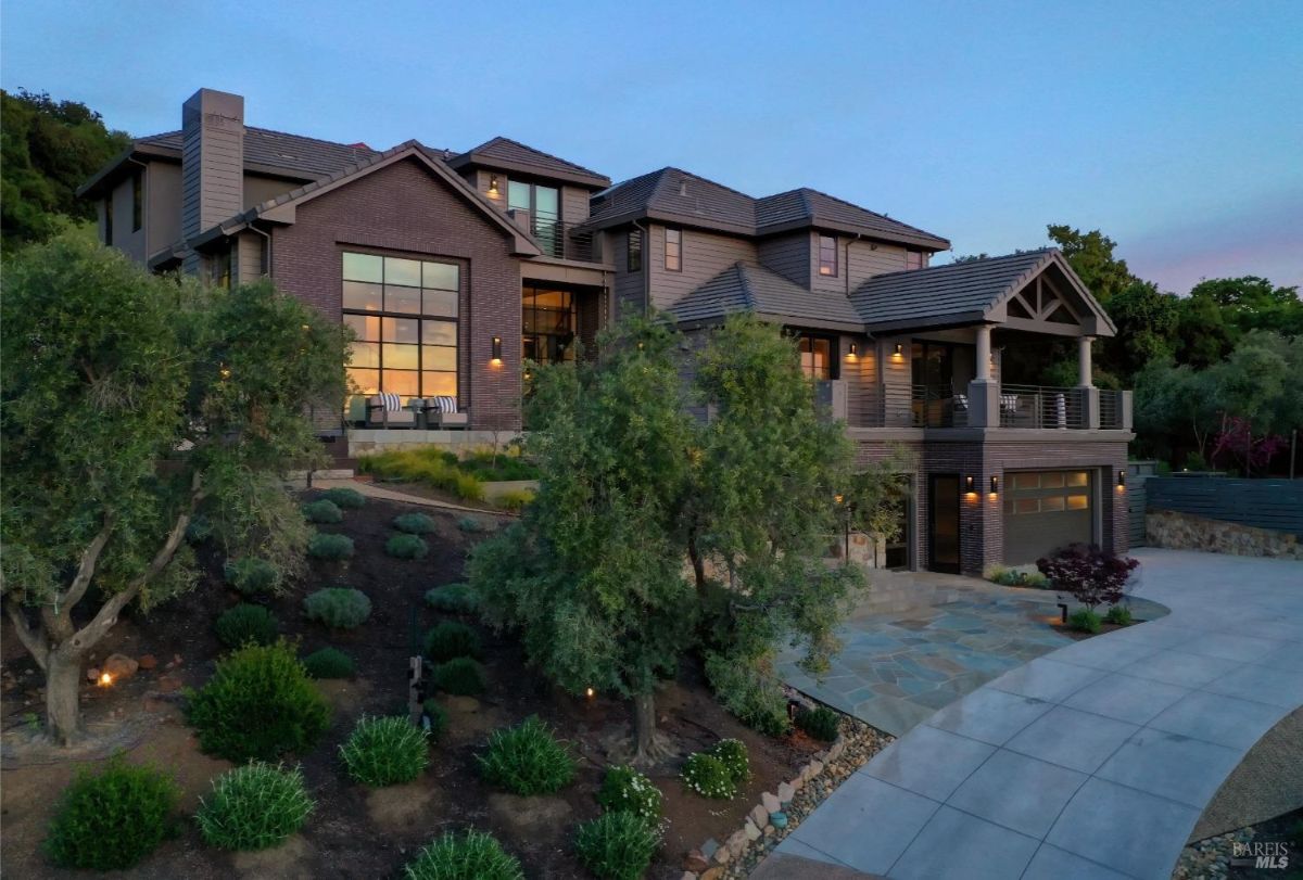 The house from a side angle, highlighting the expansive driveway, manicured landscaping, and outdoor spaces.