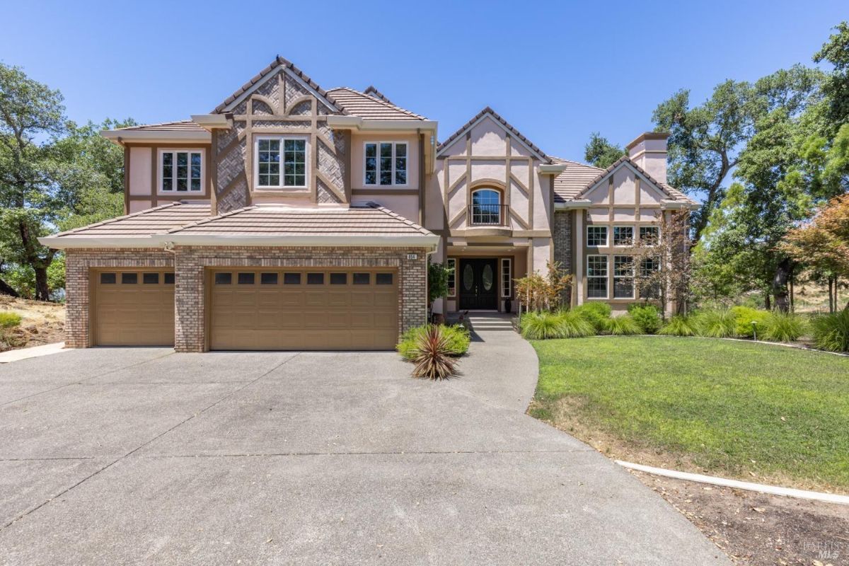 A front view of a Tudor-style home with a three-car garage, manicured landscaping, and a wide driveway.