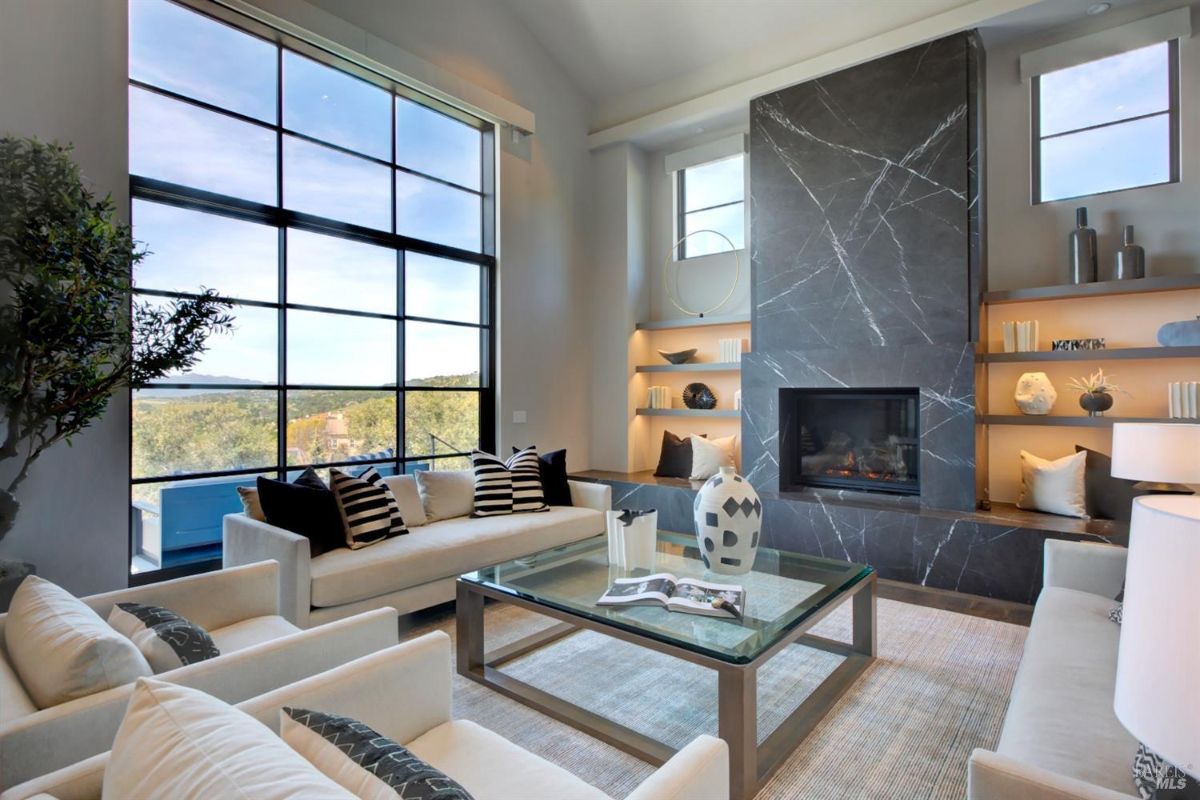 Living room with a tall black marble fireplace, built-in shelves, and large windows offering a scenic view.