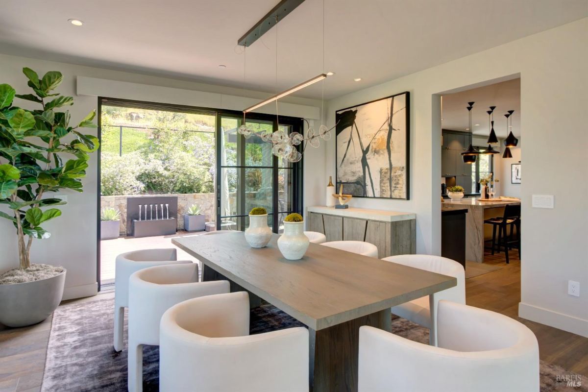 Dining room with a wooden table, white chairs, and access to an outdoor patio through sliding glass doors.