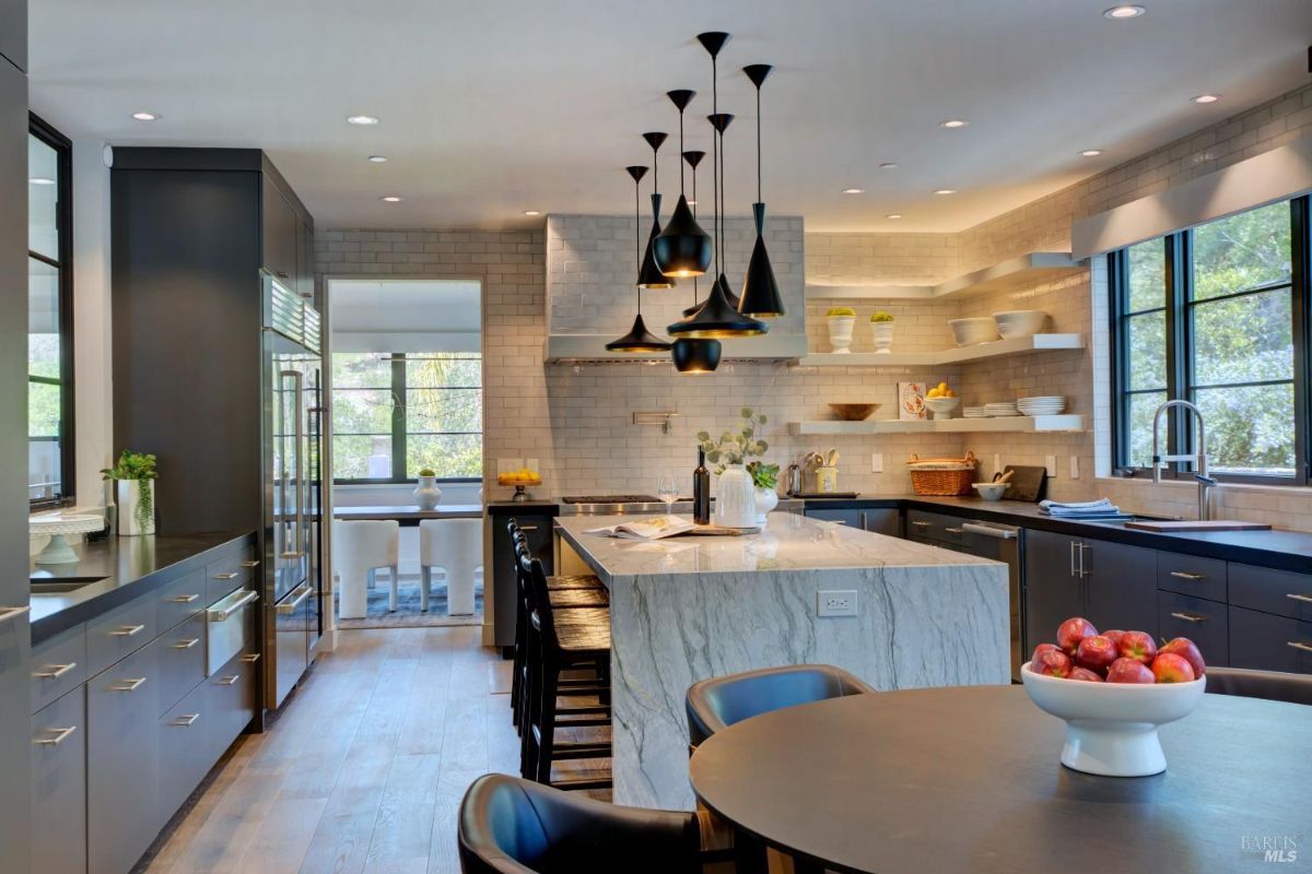 Modern kitchen with a marble island, pendant lighting, open shelving, and large windows.