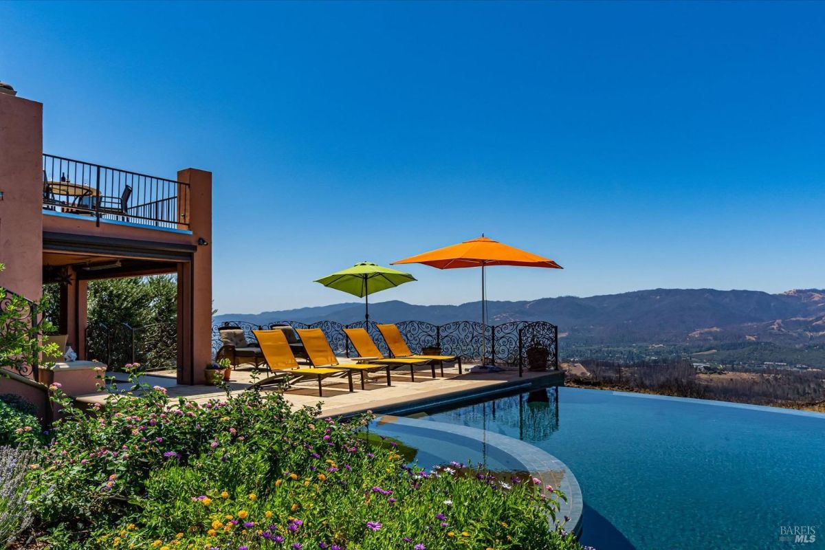 Infinity pool with lounge chairs and umbrellas facing a mountain view.