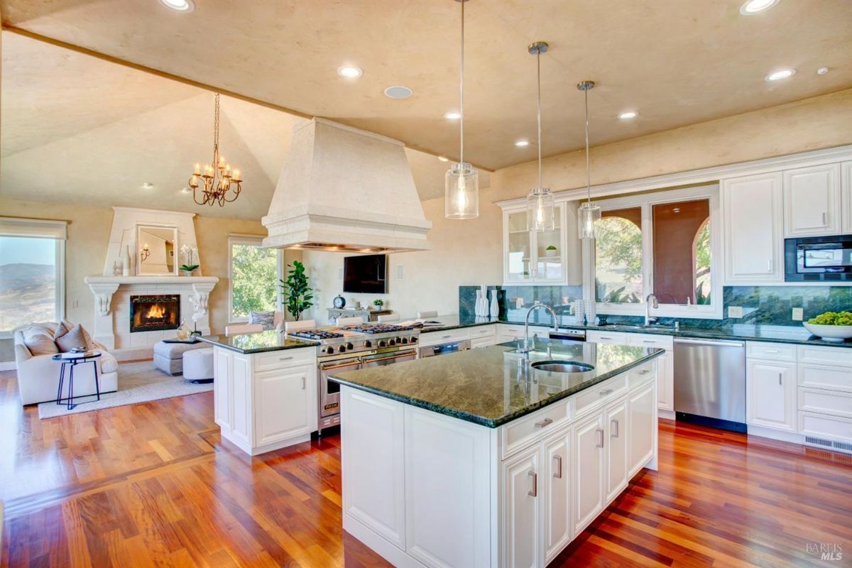 Kitchen with white cabinetry, granite countertops, a center island, and adjacent open living area featuring a fireplace.