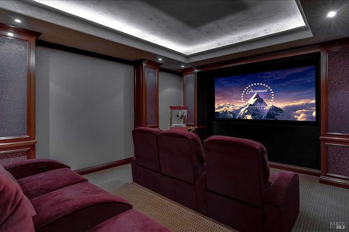 Home theater room features tiered seating with plush recliners and a large screen surrounded by dark wood paneling.