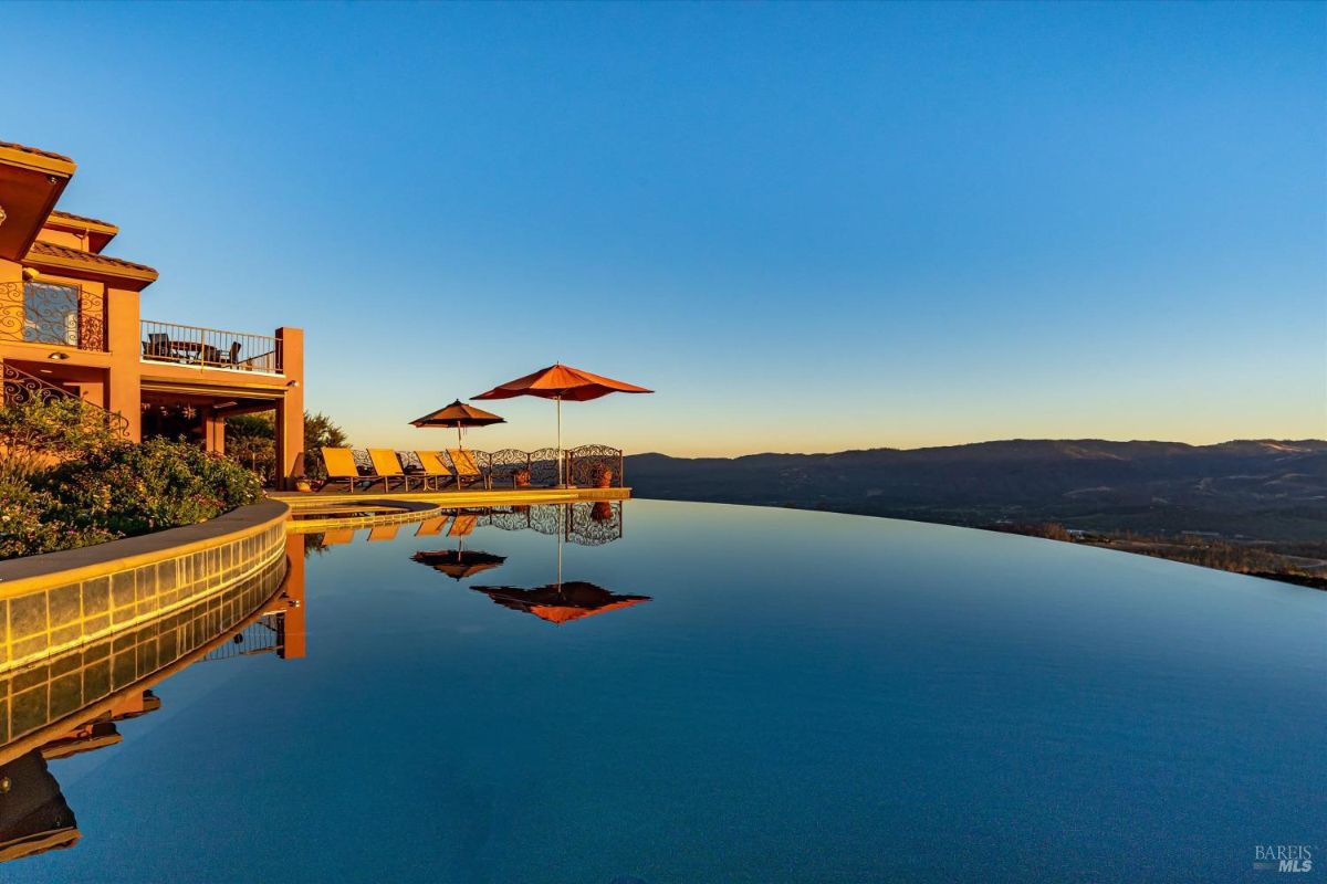 Infinity pool at sunset reflecting the surroundings with lounge chairs and umbrellas.