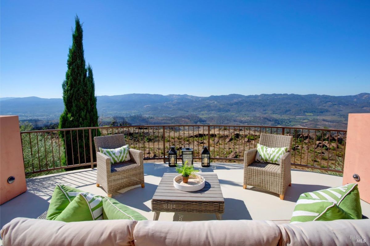 Outdoor lounge area with patio chairs and green pillows overlooking a valley landscape.