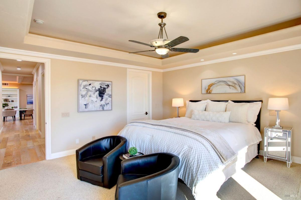 Bedroom features a white bed, black accent chairs, and wall art, with a hallway visible in the background.