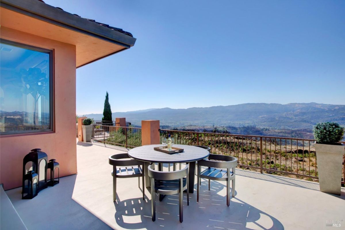 Outdoor seating area has a small round table with chairs overlooking expansive mountain views.