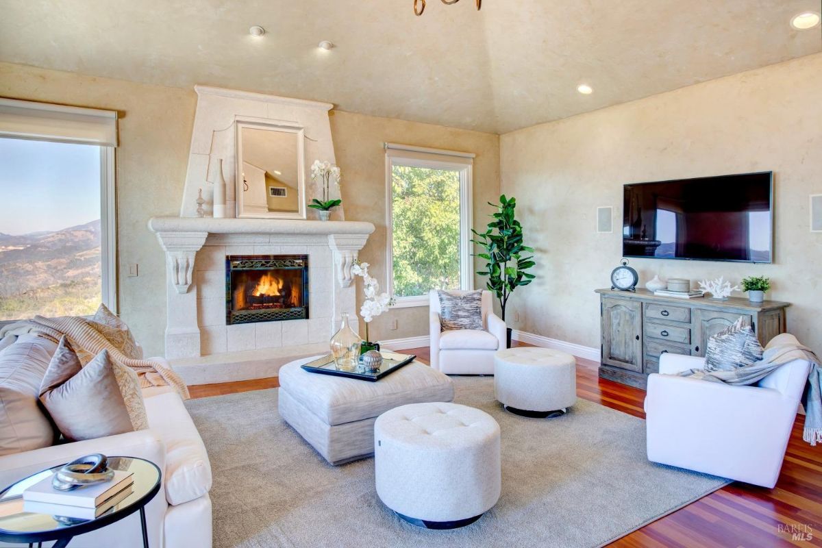 Living room with a stone fireplace, seating, and large windows overlooking greenery.