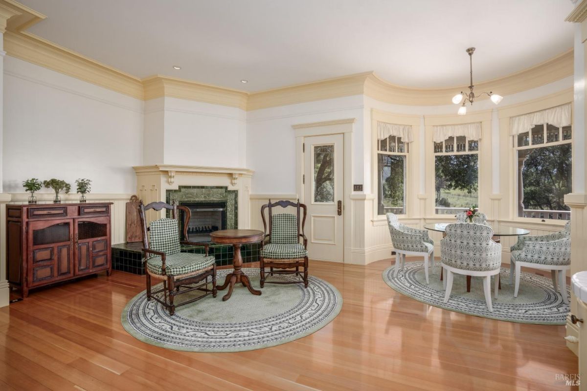 Dining nook with an attached sitting area, featuring a fireplace, hardwood floors, and vintage furniture. The light colors and natural lighting create a bright and welcoming space