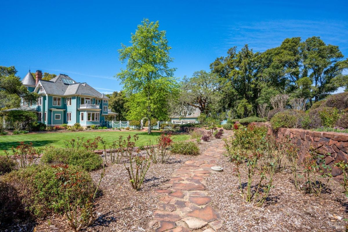 A wider perspective showing the garden's pathway and lush landscaping, with the majestic mansion in the background surrounded by mature trees and open lawns.