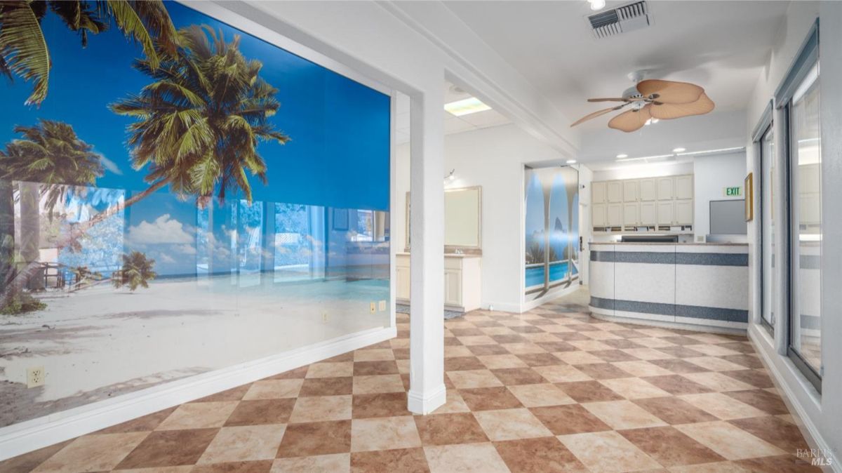 A large reception or lounge area featuring a tropical-themed wall mural of a beach scene. The tiled floor with checkered patterns and light fixtures create a bright and welcoming ambiance.