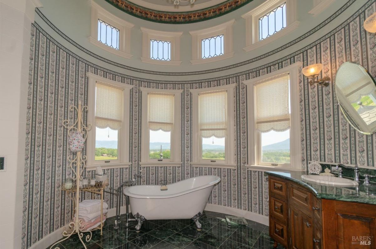 Elegant bathroom with a freestanding tub surrounded by windows and intricate wallpaper design.