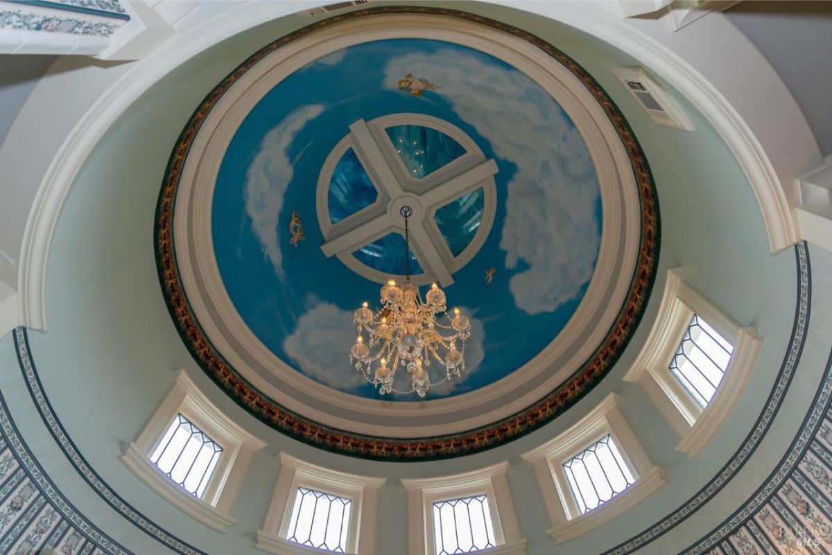 Ornate dome ceiling featuring sky artwork and a chandelier with surrounding windows.