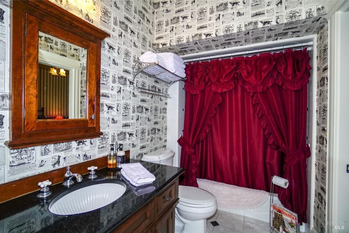 Vibrant bathroom with red curtains and vintage newspaper-style wallpaper.