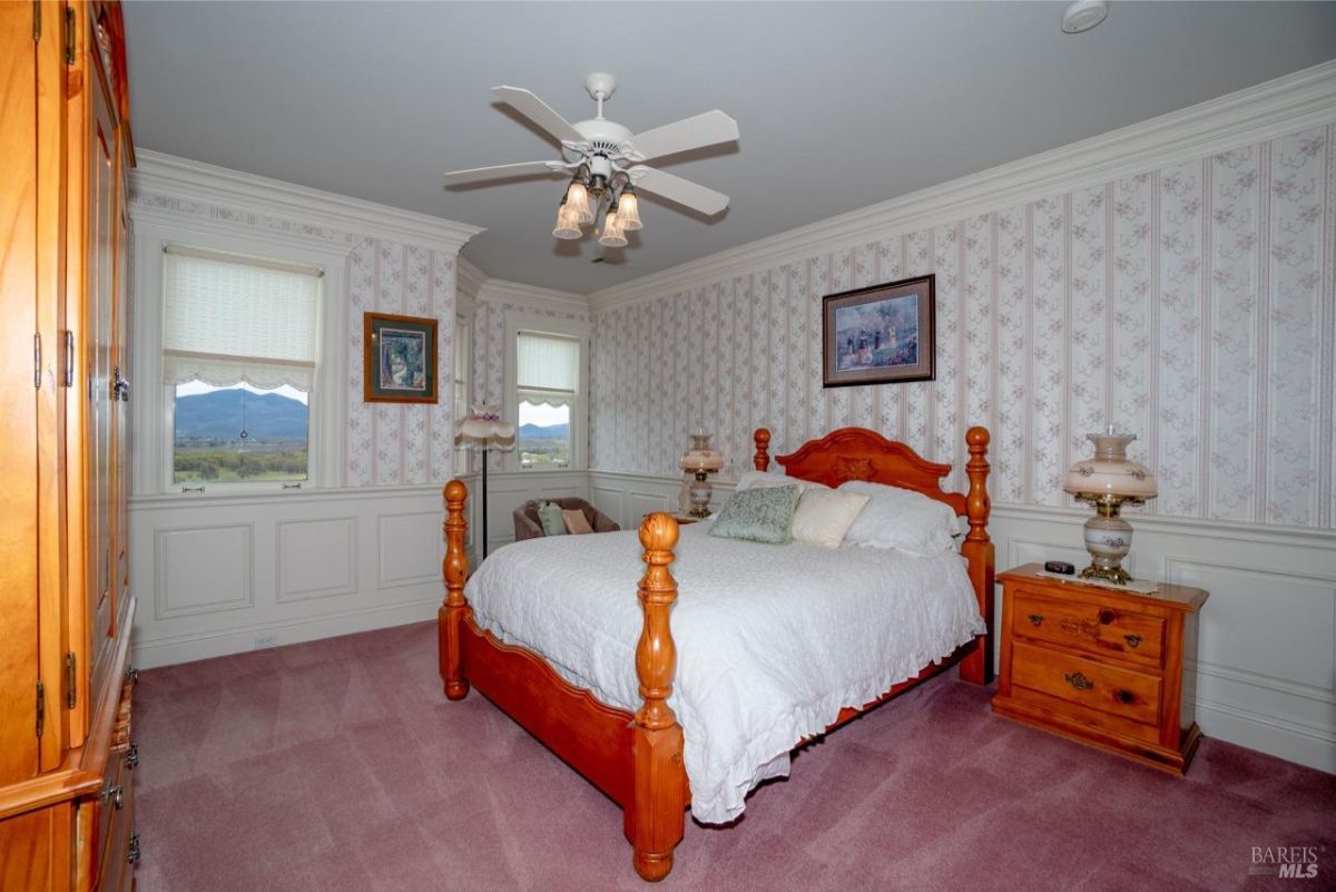 Bright bedroom with wooden furniture, pink carpet, and large windows with scenic views.