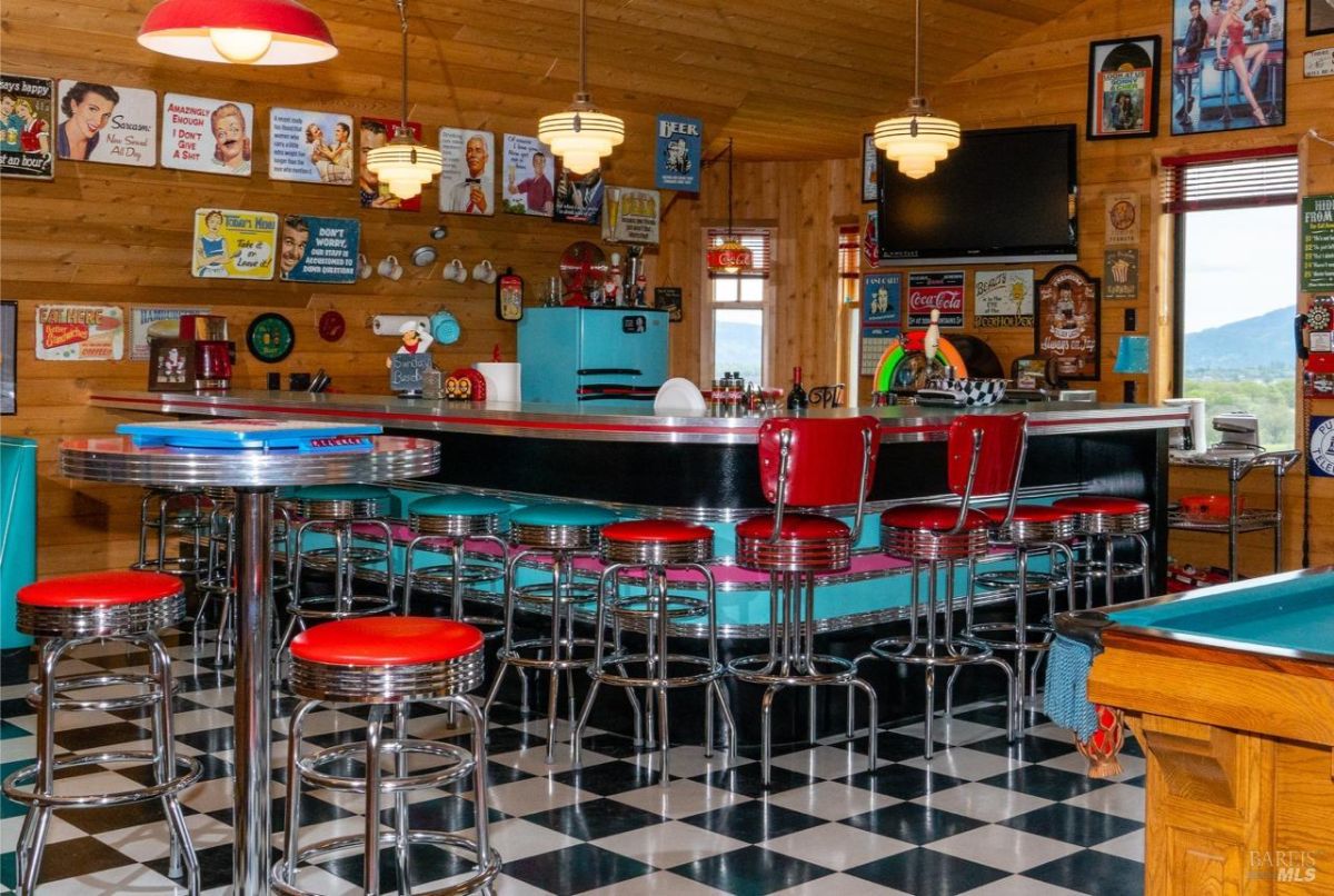 Retro diner-themed entertainment room featuring a bar with red stools and vintage decor.