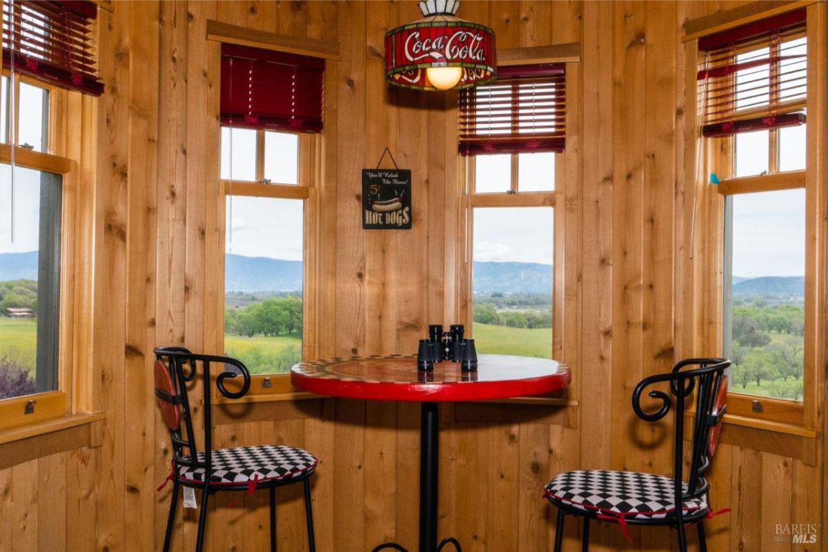 Cozy corner seating area with a red table and a Coca-Cola theme surrounded by windows offering a panoramic view.