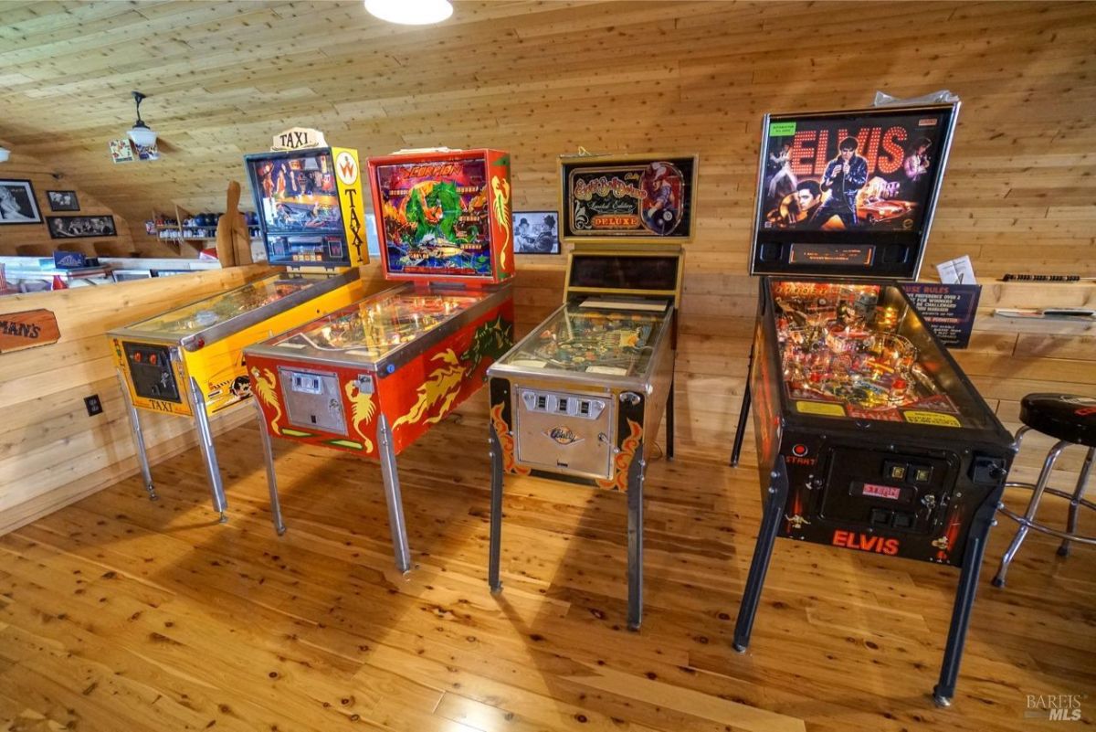 Display of colorful pinball machines in a neatly arranged layout on polished wooden flooring.