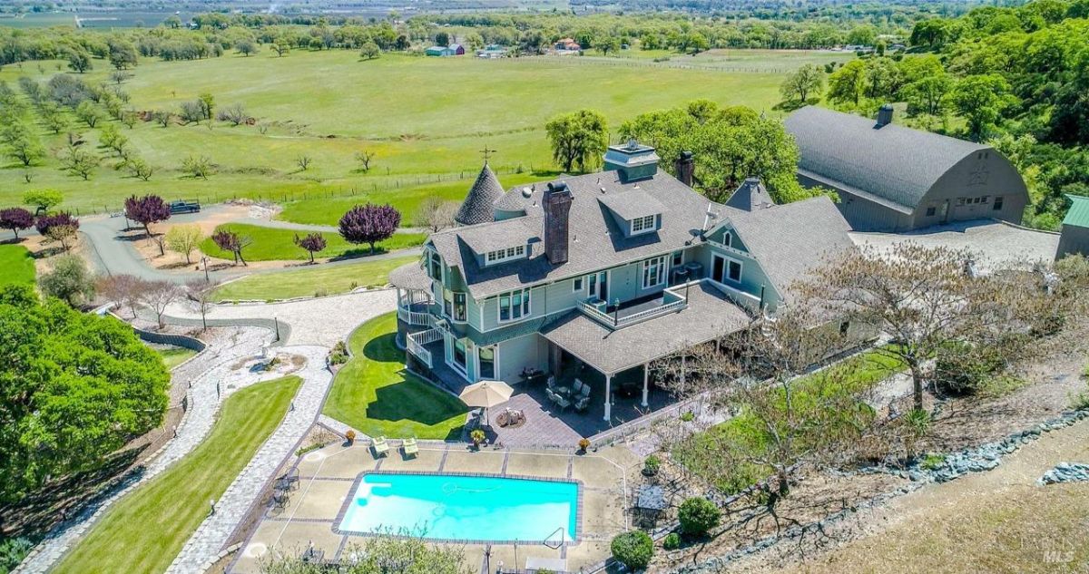 Rear aerial view of the estate highlighting the pool, patio, and open landscape.