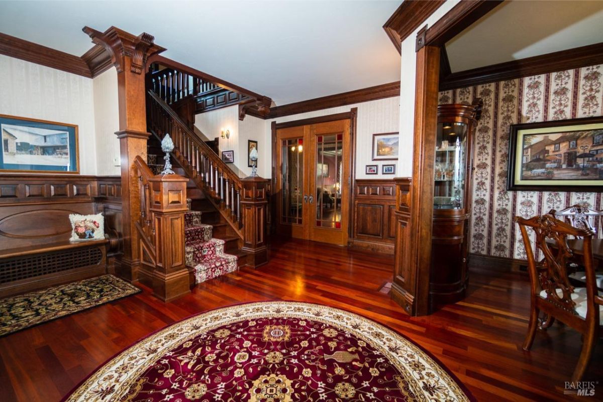 Elegant entryway with rich wooden staircases, stained glass accents, and vibrant rugs.