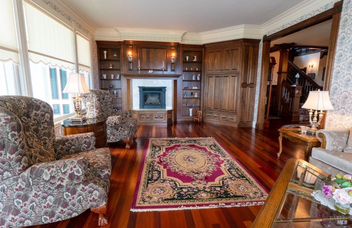 Cozy lounge area with a fireplace, built-in wooden shelves, and ornate floral-patterned chairs.