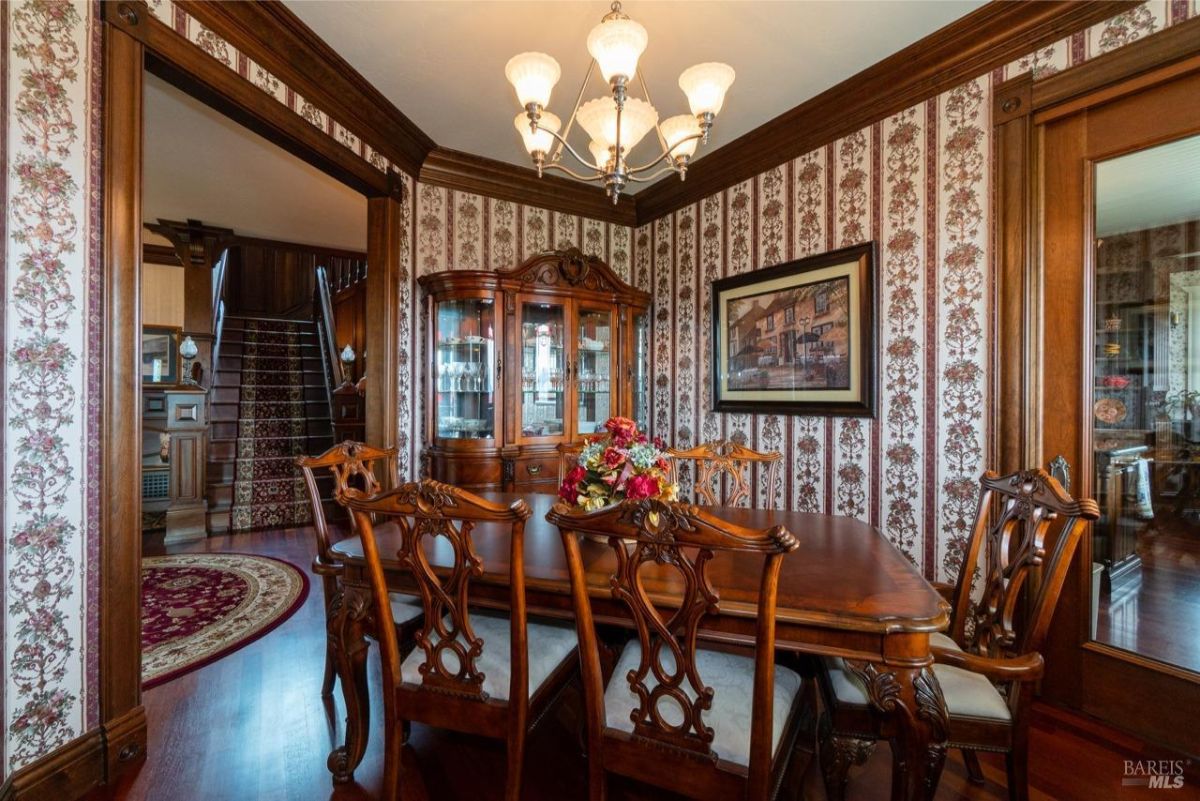 Elegant dining room with floral wallpaper and a chandelier above a polished wooden table.