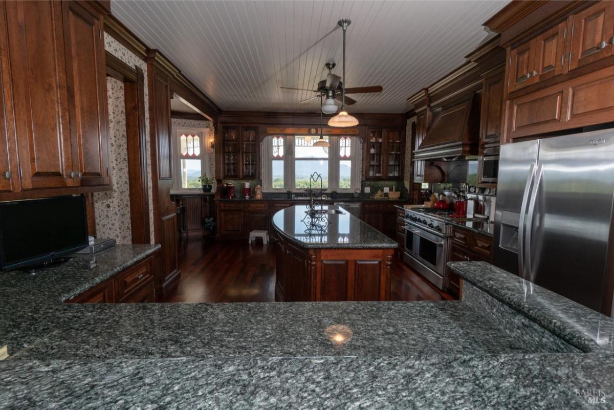 Spacious kitchen with dark wooden cabinets, granite countertops, and a central island beneath a ceiling fan.