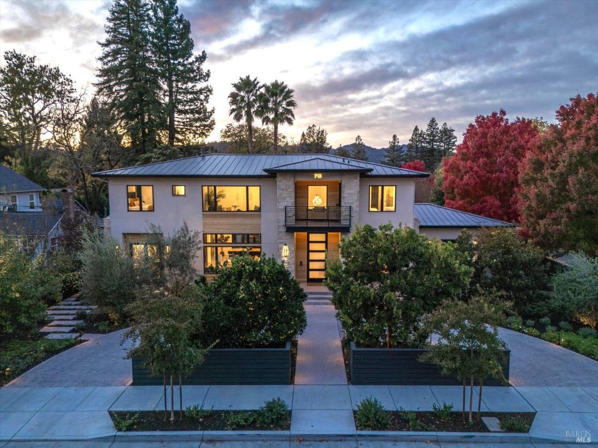 Modern two-story home surrounded by landscaping, captured at dusk with interior lights on.