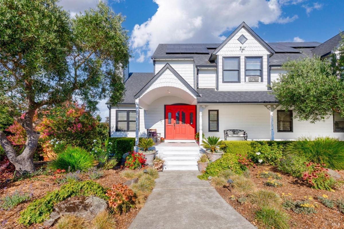 White two-story house with a red front door, multiple windows, and a wraparound porch.