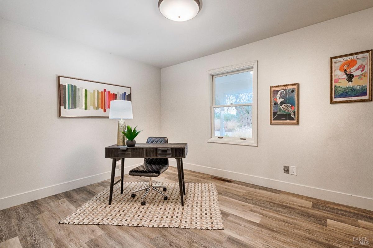 Wood flooring, a desk, a chair, a lamp, and artwork on the walls.