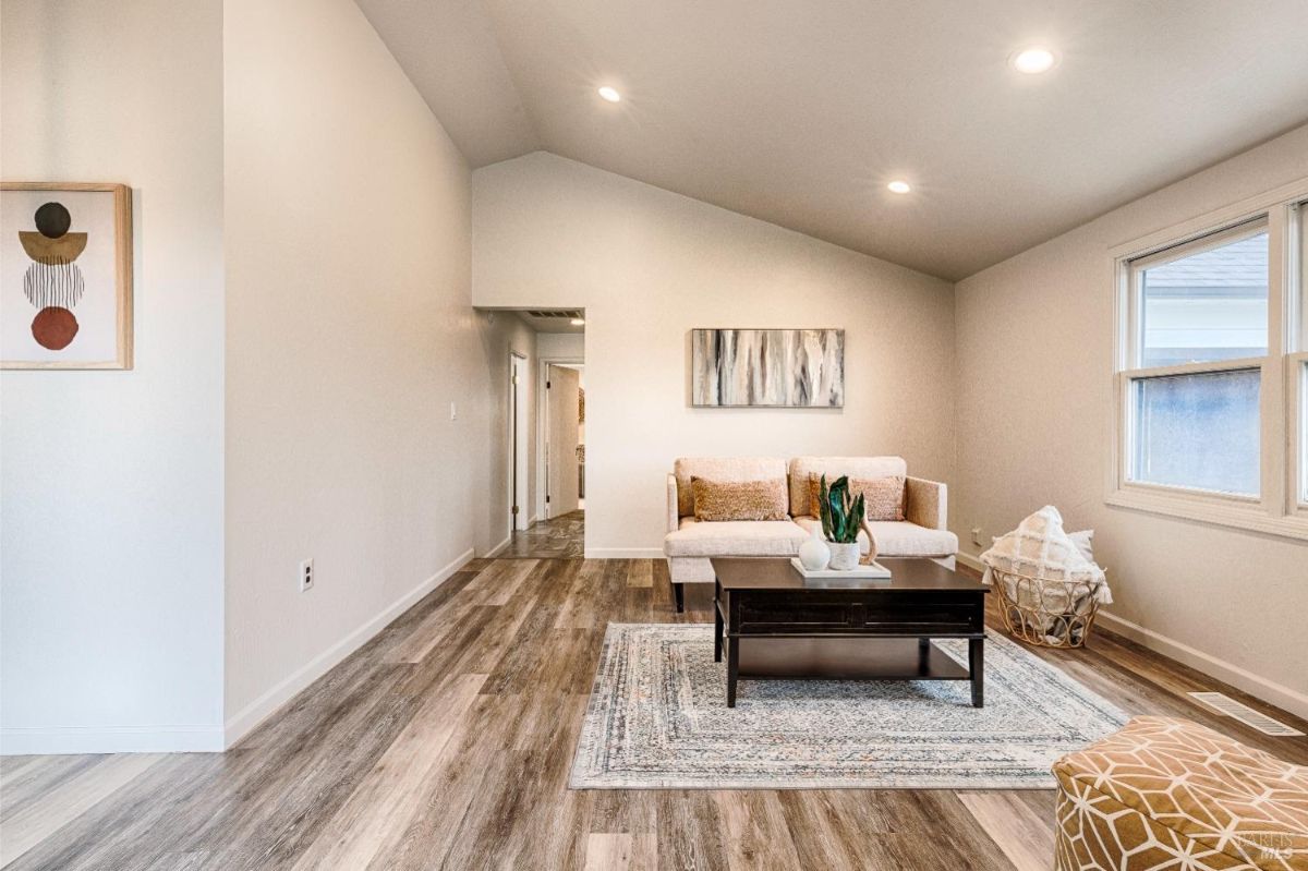 Vaulted ceiling, wood flooring, a sofa, a coffee table, and a doorway leading to another room.