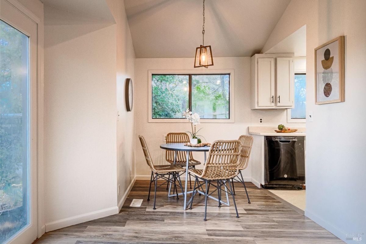 Dining table with four chairs, a hanging light fixture, and a view of a kitchen.