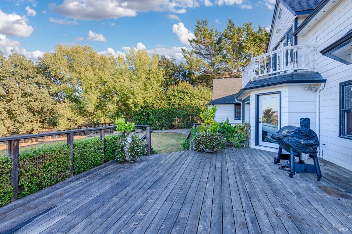 Wood deck with a view of a backyard and a grill.