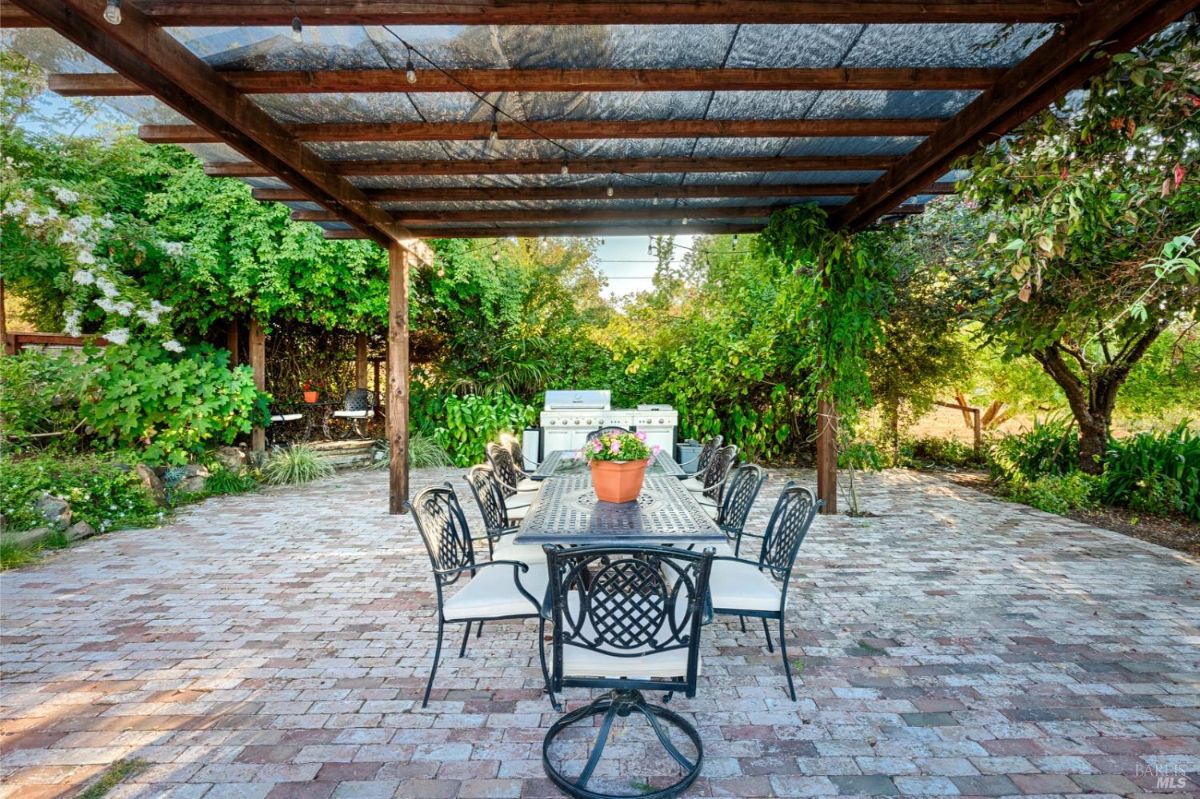 Brick patio with a pergola, outdoor dining table and chairs, and a grill.