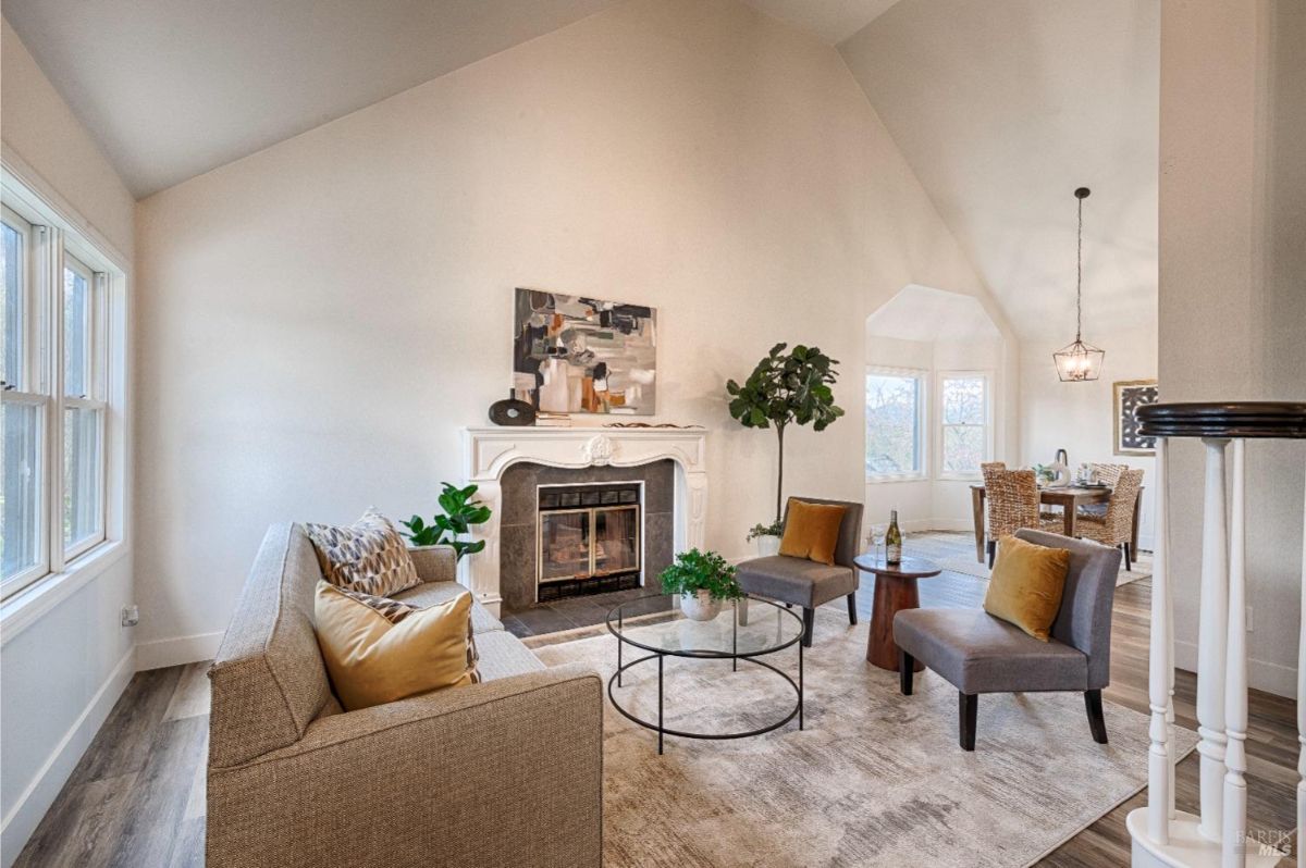 Vaulted ceiling, fireplace, two armchairs, a sofa, a coffee table, and a view of a dining room.