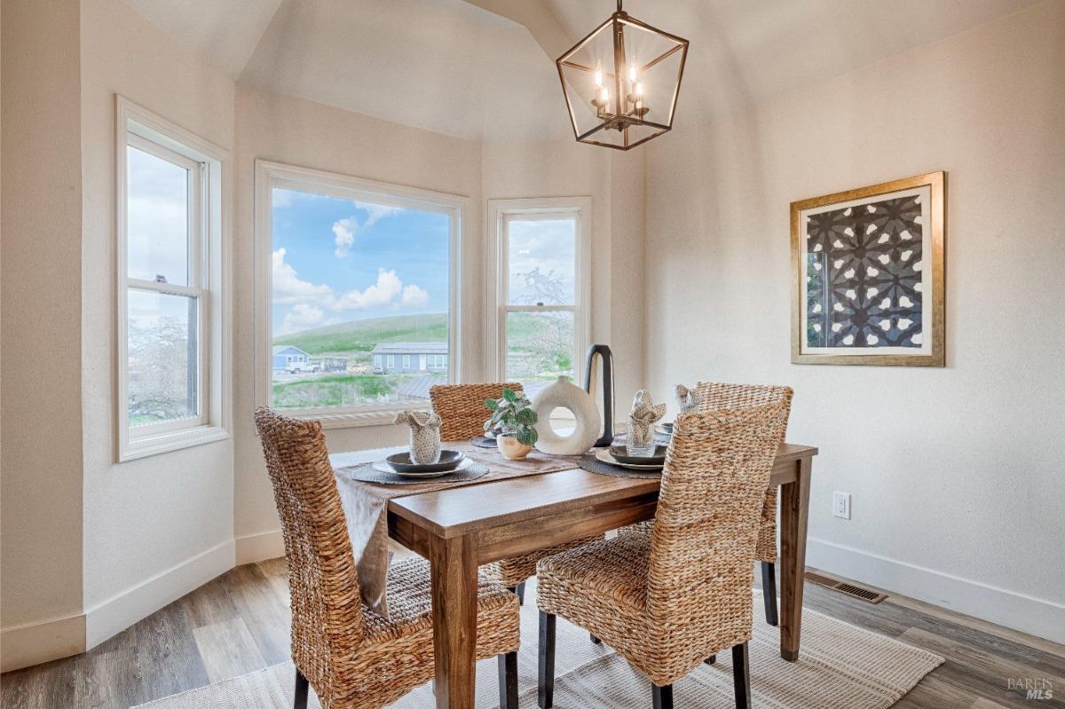 Dining table with four chairs, a large window with a view, and a hanging light fixture.