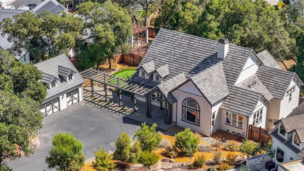 Modern house with a gray tile roof and a detached garage surrounded by lush trees.