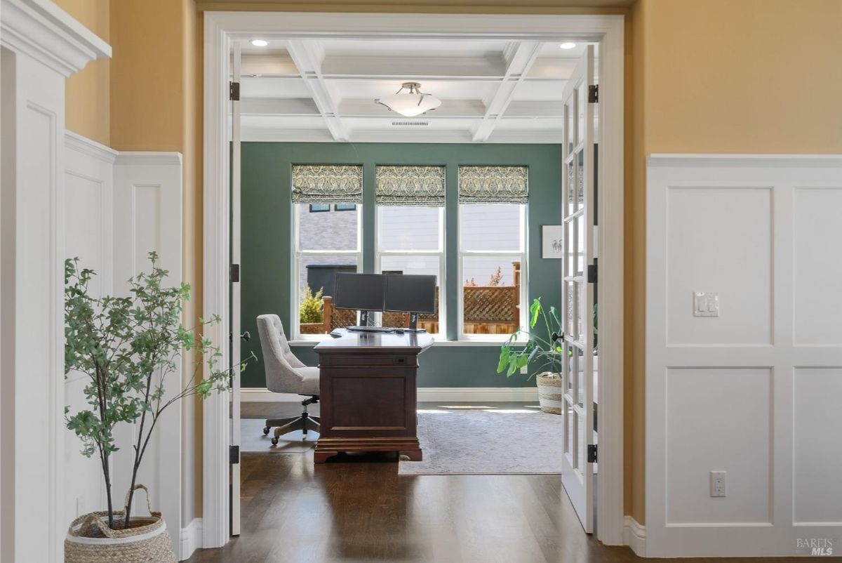 Stylish home office with green walls, large windows, and a traditional wooden desk.