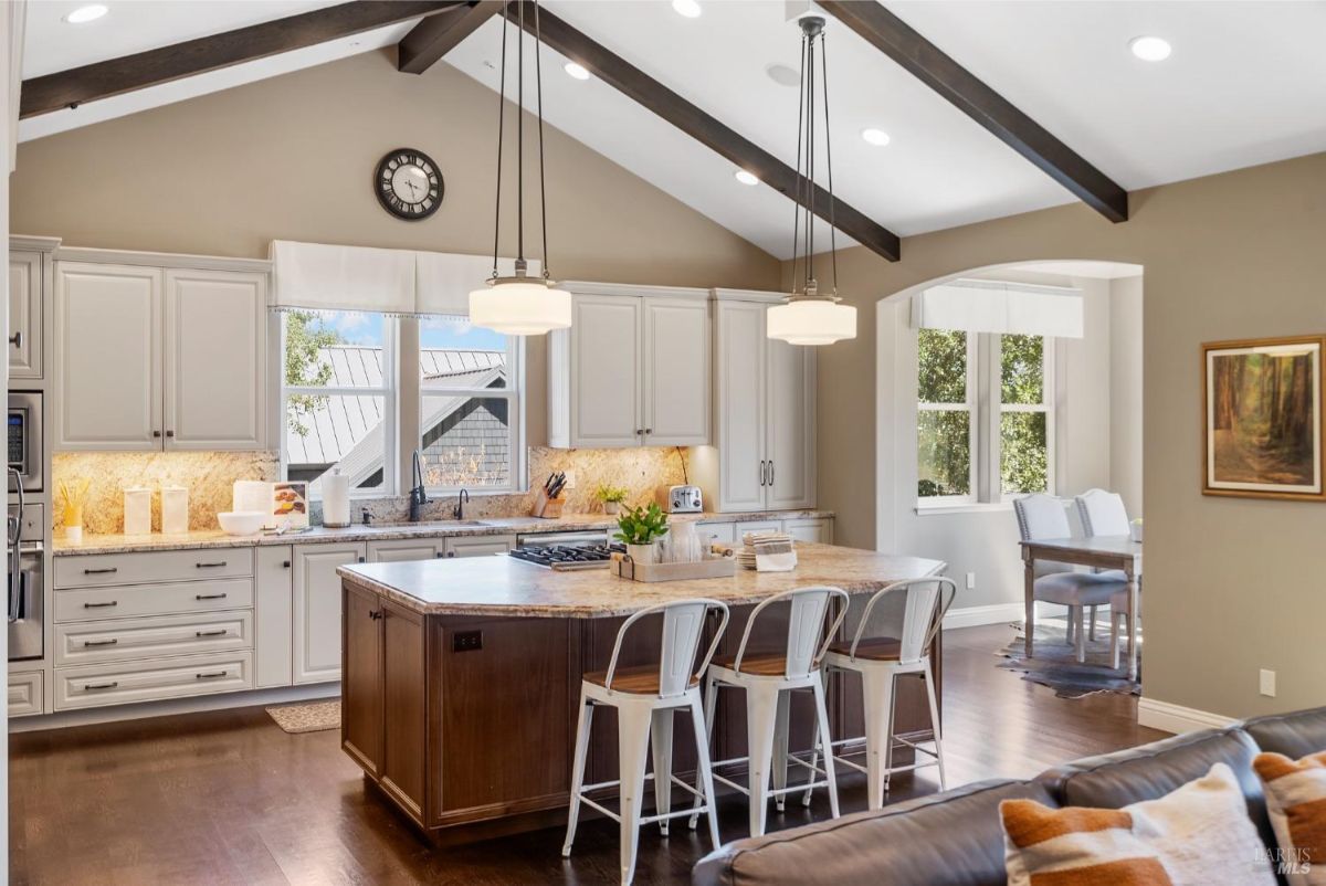 Kitchen showcases white cabinets, a large island with pendant lights, and exposed wooden beams on the ceiling.