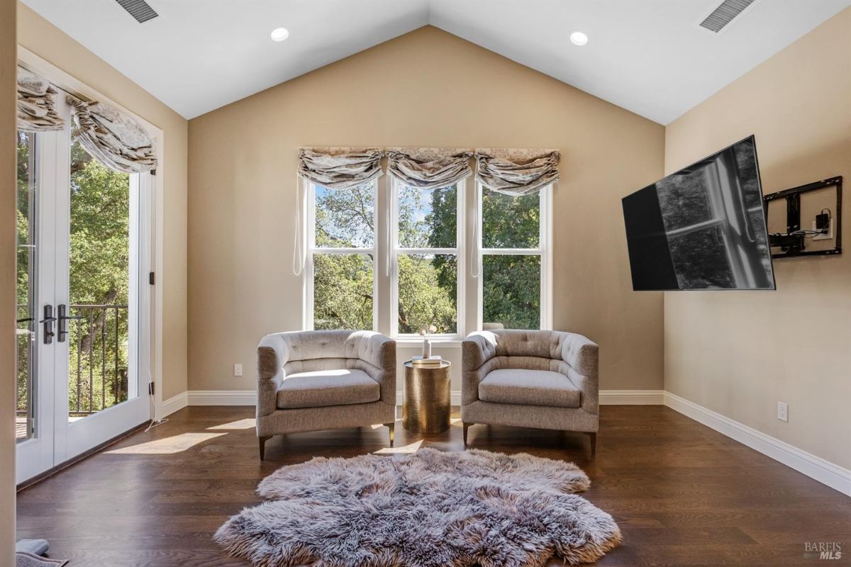 Elegant sitting area with vaulted ceilings, soft armchairs, and a plush rug under a wall-mounted TV.