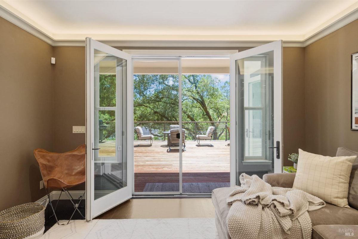 Bright living room with French doors opening onto a serene deck with outdoor seating.