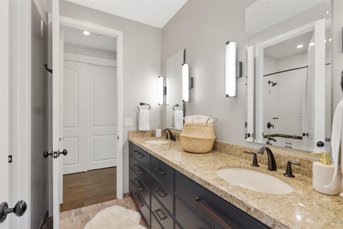 Bathroom with dual sinks, granite countertops, and a shower visible through the open door.